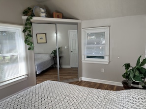 Un dormitorio con cama, ventana, puerta y espejo.