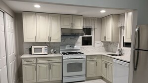 A kitchen with white cabinets, a gas stove, a microwave, and a refrigerator. - Entire 3 bedrooms/2 bathrooms fence yard, near Costco, Sam's (Gaithersburg)
