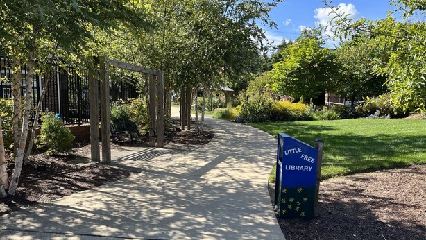 A pathway leading to a Little Free Library, surrounded by trees and greenery. - Entire 3 bedrooms/2 bathrooms fence yard, near Costco, Sam's (Gaithersburg)