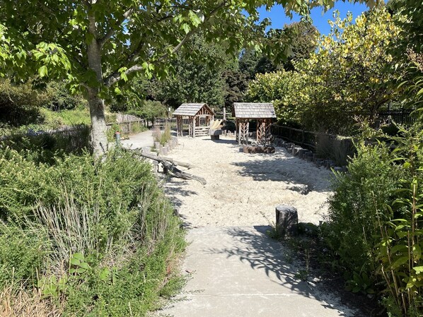 A pathway leading to a rustic wooden structure with a thatched roof, surrounded by dense greenery and trees.