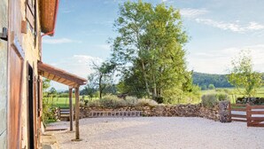 Ein Stall mit Kiesfläche, Steinmauer, Holzpferd und Bäumen im Hintergrund.