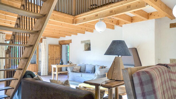 Ein rustikales Interieur mit sichtbaren Holzbalken, einer Treppe, einem Sofa, einem Tisch und einer Lampe.