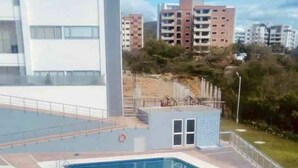 Une piscine entourée d’une promenade, un petit bâtiment annexe et, en arrière-plan, une vue sur des immeubles d’habitation.