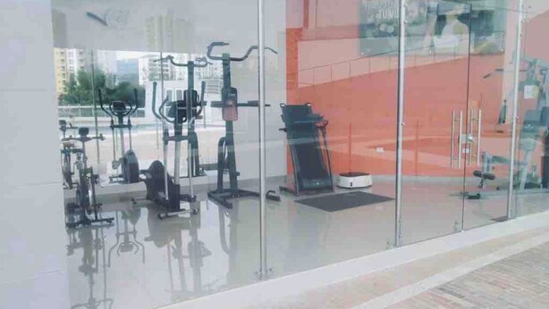 Une salle de sport moderne, dotée de divers appareils d’exercice, notamment des tapis de course et des vélos d’appartement, que l’on peut apercevoir à travers une paroi en verre.