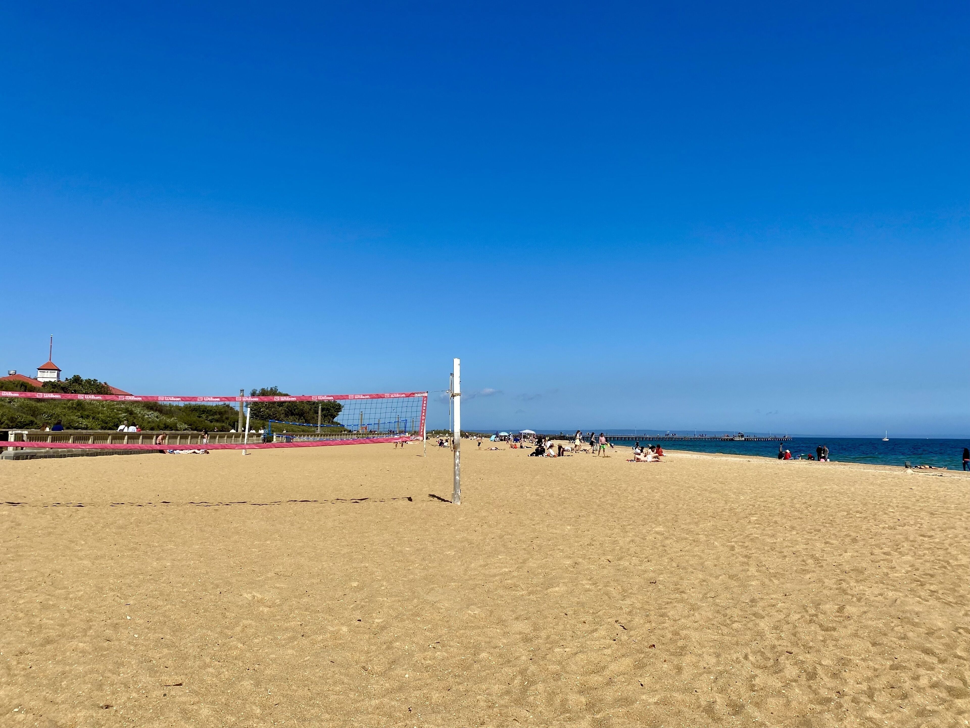 A beach volleyball court with a net, sandy beach, and a clear blue sky.