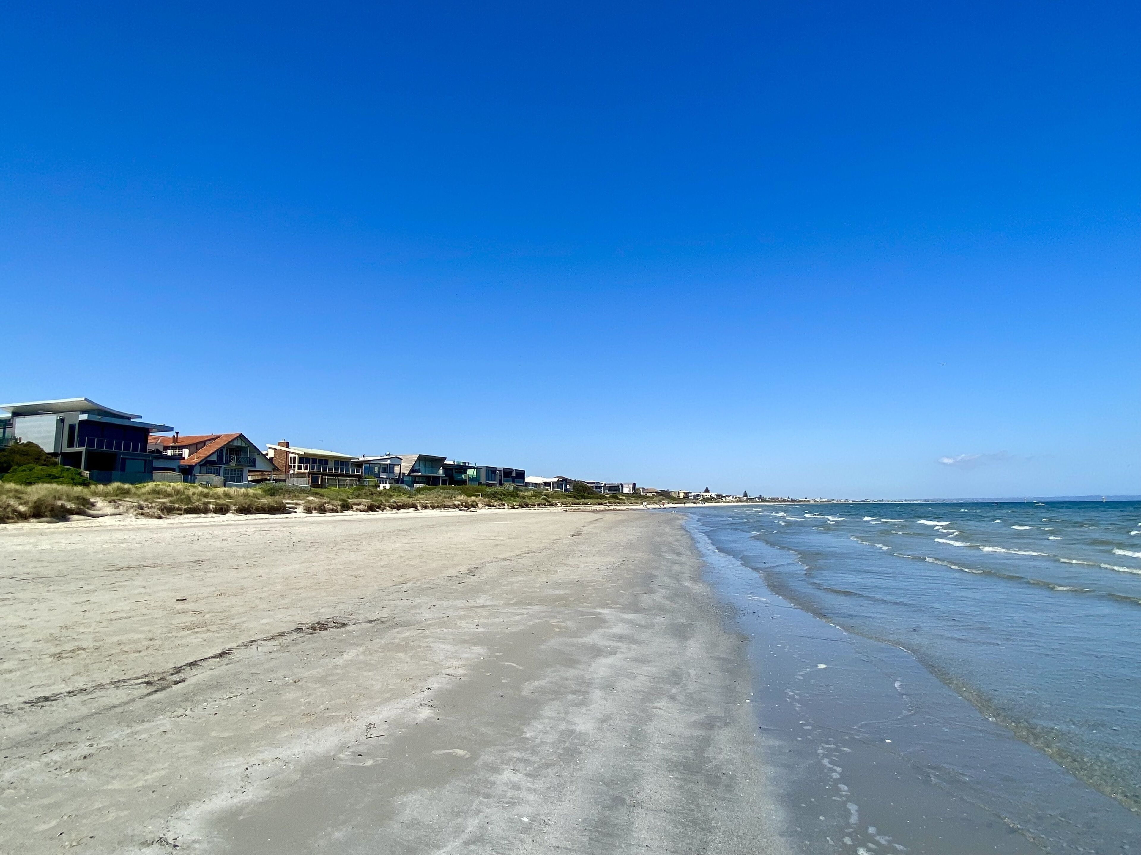 En strand med moderne bygninger, sandet bredde og klar blå himmel.