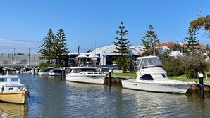 A marina with several boats docked, a building with a white roof, and a clear blue sky. - Beach Rd | Kids & Pet Friendly | Free Parking (Mordialloc)