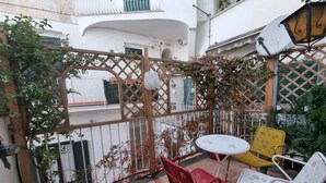Un patio con una verja de madera enrejada, una pequeña mesa redonda con dos sillas y plantas en macetas.