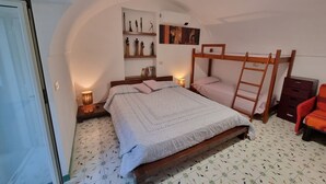 Un dormitorio con una cama nido, una mesita de noche con lámpara, una estantería con objetos decorativos y un aire acondicionado de pared.