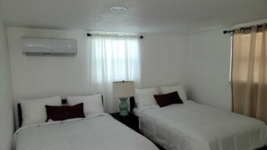 Une chambre d’hôtel avec deux lits, une fenêtre avec des rideaux légers, un climatiseur fixé au mur et une lampe de chevet.