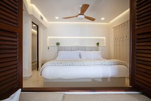 A modern bedroom with a large bed, a ceiling fan, recessed lighting, and a decorative wall panel.