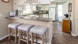 Una cocina con una isla central, taburetes de bar, armarios blancos, un microondas y un refrigerador.