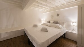 Une chambre avec un plancher en bois, un lit recouvert de draps blancs, une lucarne et une décoration en forme de cœur sur le mur.