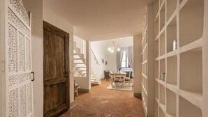 Un couloir avec une porte en bois, un escalier, un coin repas avec une table et des chaises, et une étagère.