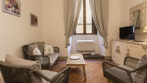 Un salon avec un canapé, des fauteuils, une table, un téléviseur et une fenêtre avec des rideaux.