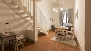 Un escalier menant à une salle à manger équipée d’une table et de chaises, d’un lustre et d’une fenêtre avec des rideaux.