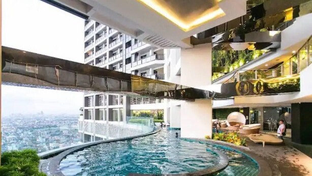 A modern indoor pool with a curved design, surrounded by lush greenery and a city view. - Makati - Sleeps 2 - Pool - Cinema - Gym - Garden (Makati)