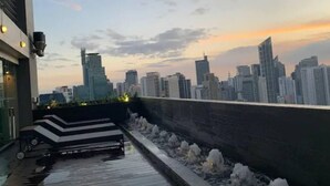 A rooftop terrace with a city skyline view, a modern building facade, and a stone retaining wall. - Makati - Sleeps 2 - Pool - Cinema - Gym - Garden (Makati)