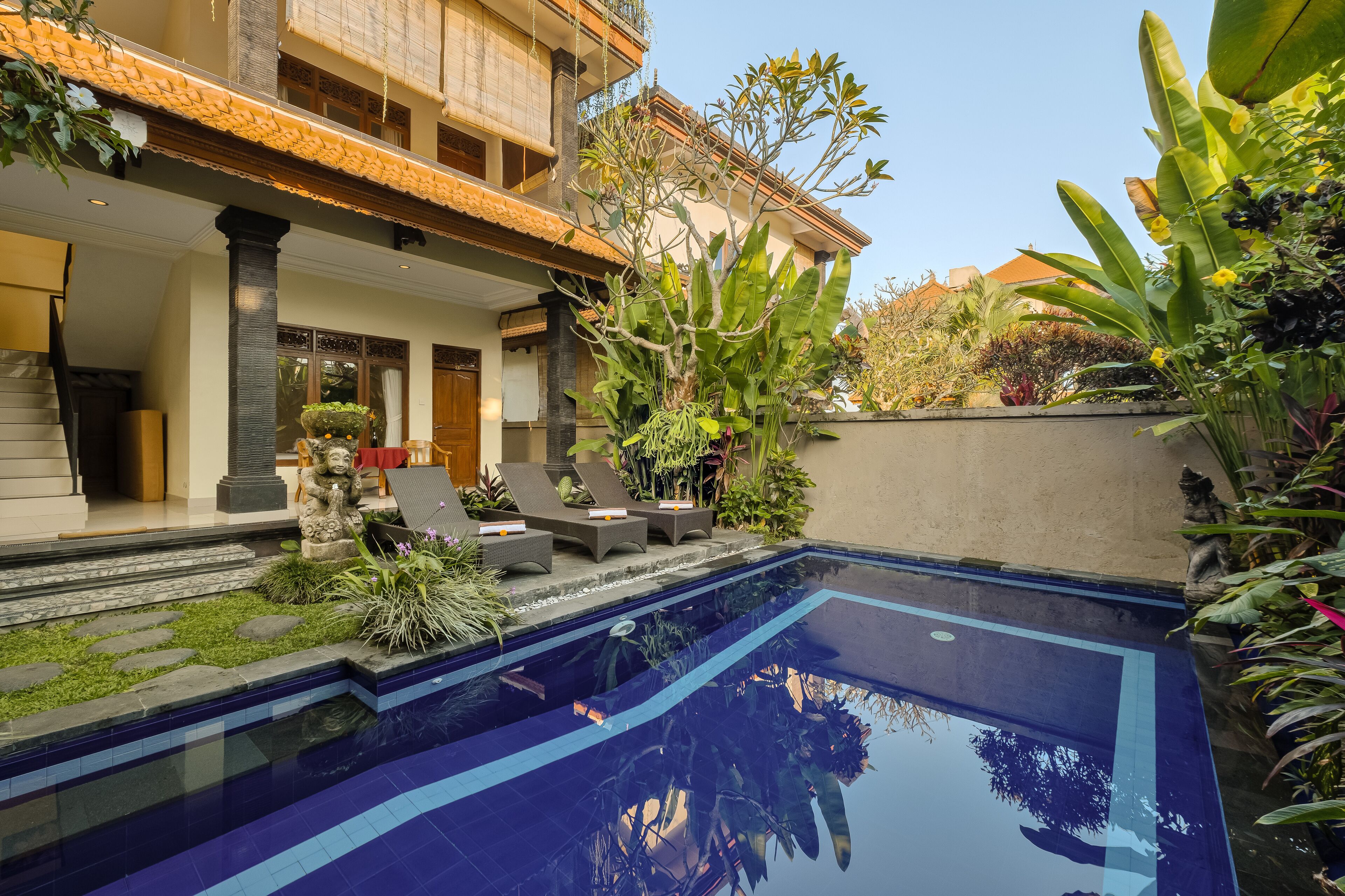 Una piscina con borde de azulejos, rodeada de plantas y un camino de piedra.