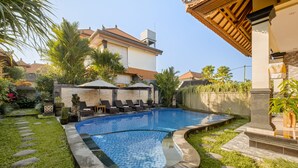 A swimming pool with a curved edge, surrounded by a well-maintained lawn and stone pathway. - Gora House Bali (Ubud)
