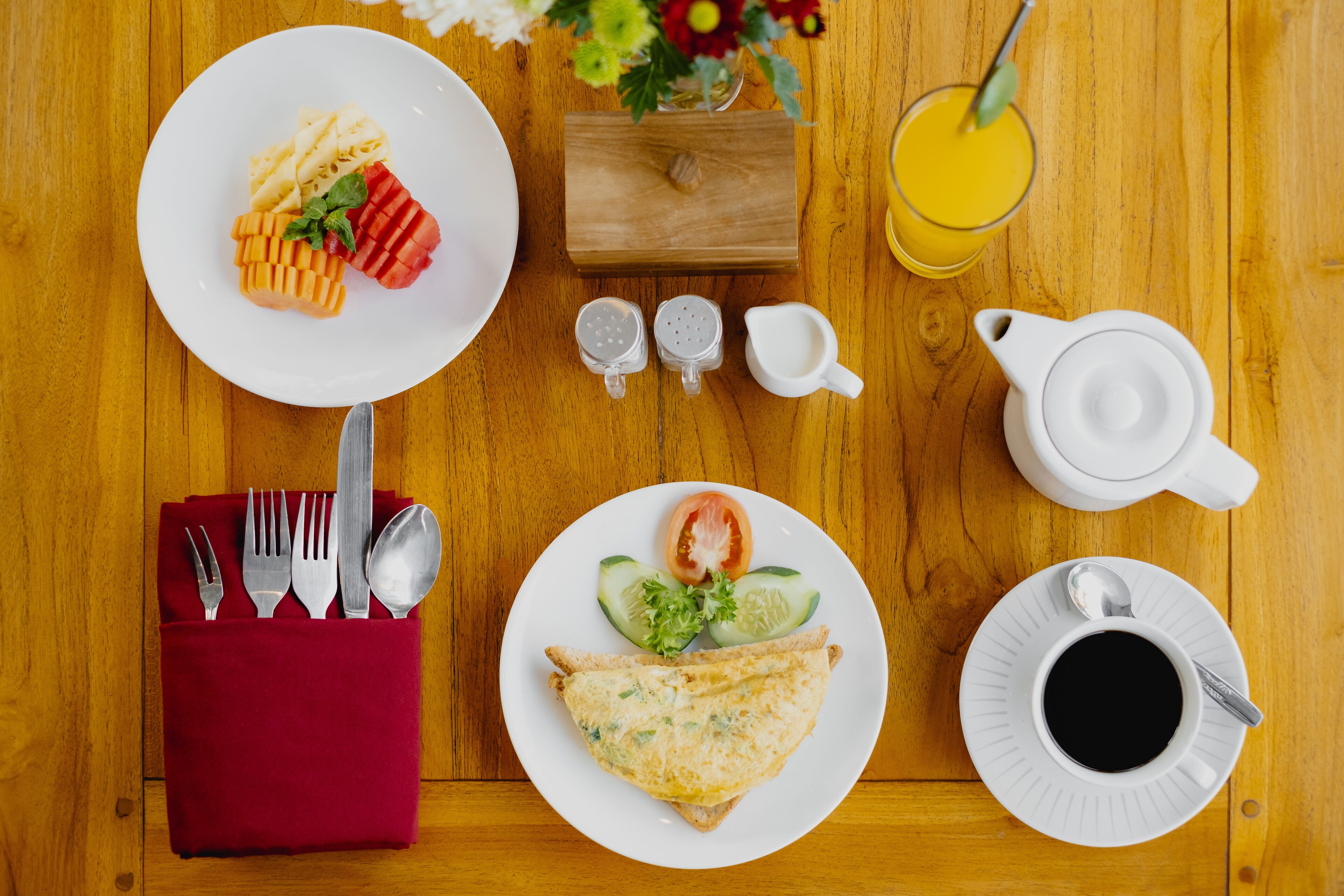 A wooden table with a breakfast setting including plates, cutlery, a teapot, and a glass of orange juice.