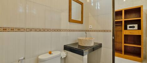 Un baño con inodoro, lavamanos, espejo y estantería de madera.