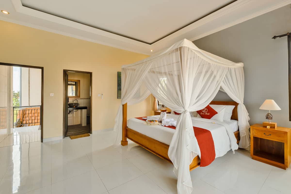 A spacious bedroom with a four-poster bed, a bedside table with a lamp, and a view of the balcony.