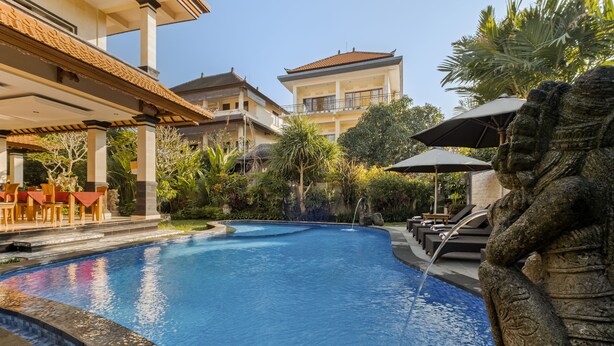 A swimming pool with a stone sculpture, outdoor seating, and a building with a tiled roof. - Gora House Bali (Ubud)