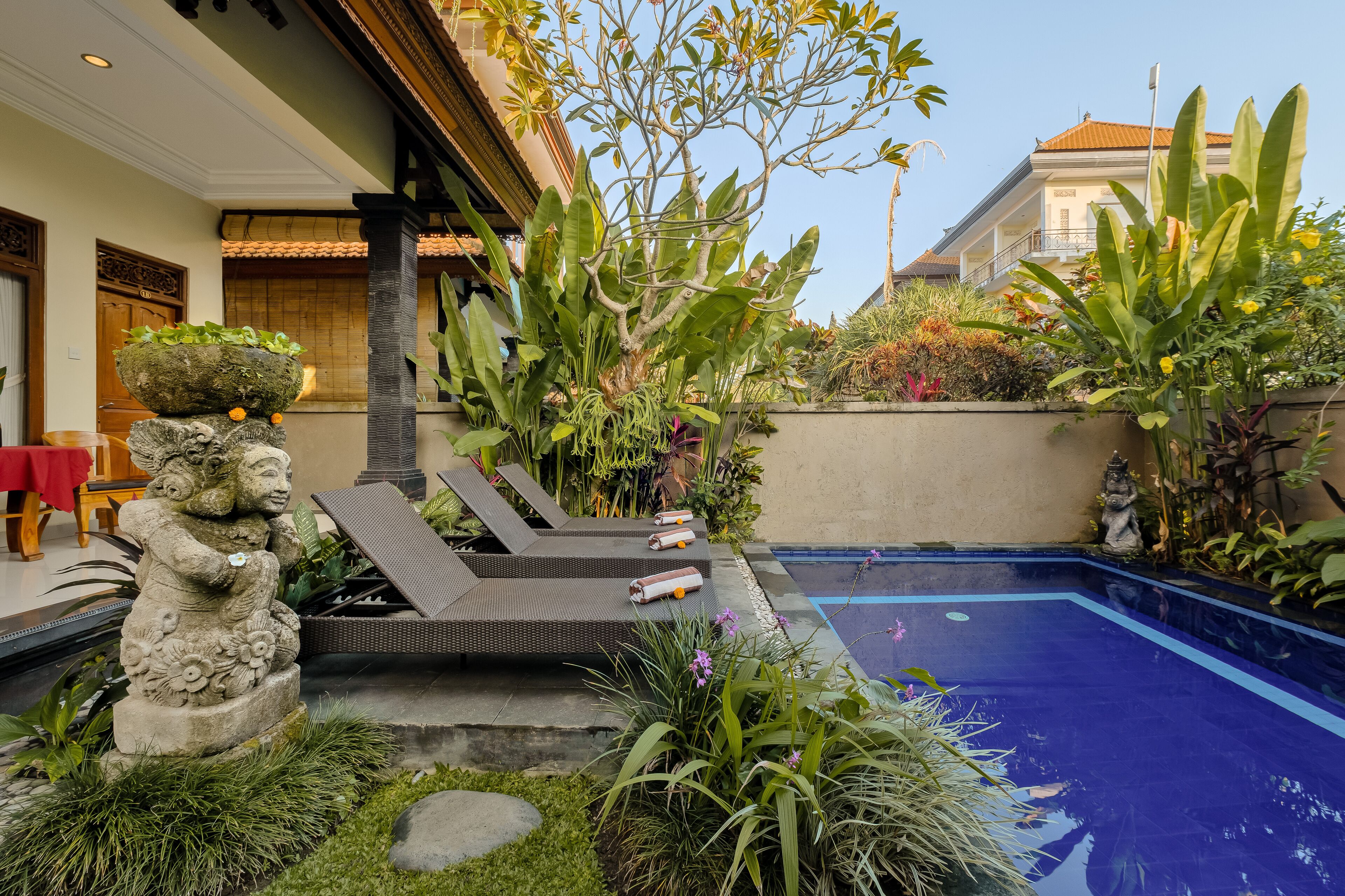 A pool area with lounge chairs, a stone statue, and lush greenery.