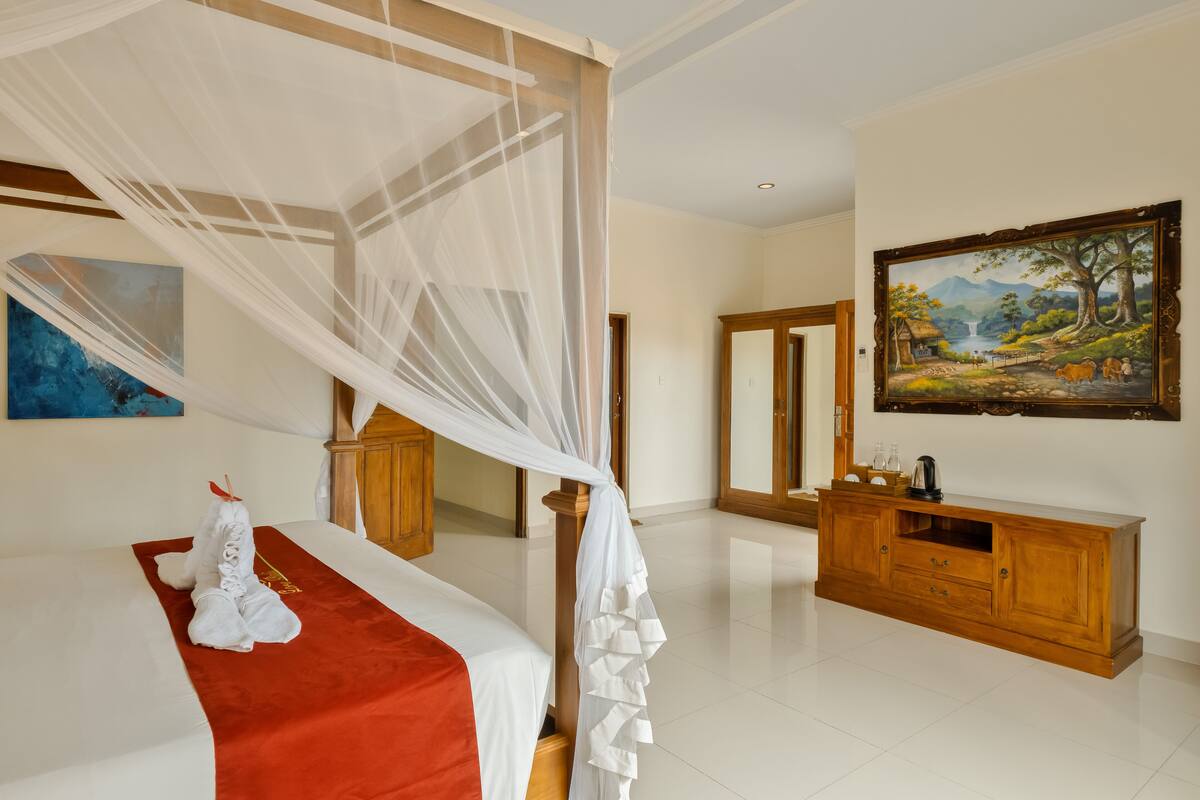 A bedroom with a canopy bed, a wooden dresser, a painting, and a mirror.