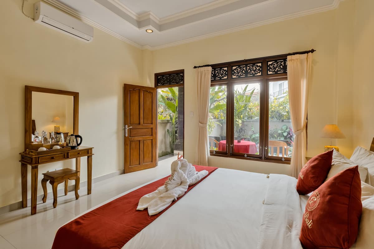 A hotel room with a bed, a wooden desk, a mirror, and a window with curtains.