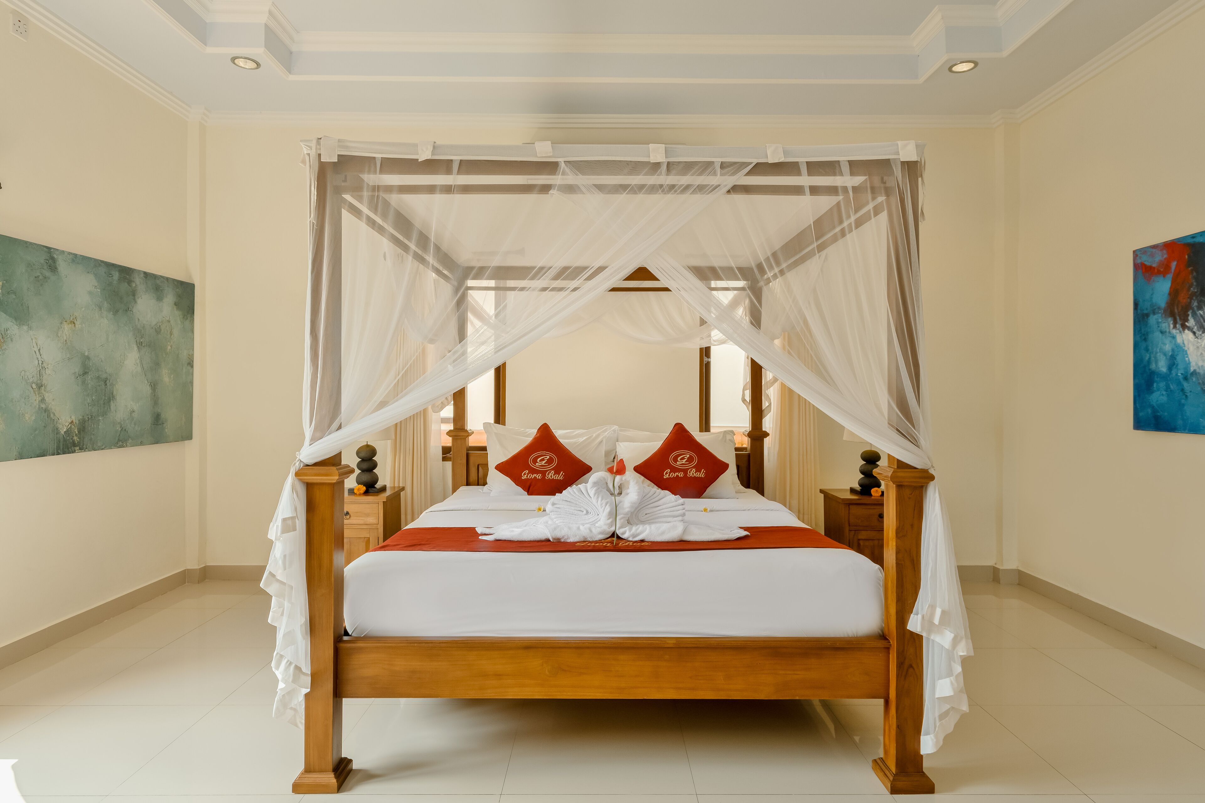 A neatly made bed with a canopy, two pillows with a logo, and a bedside table with a lamp.