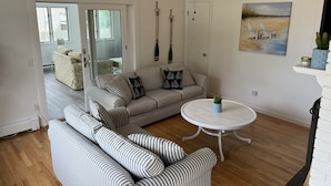 A living room with striped sofas, a round table, and a beach painting on the wall. - Beach Cottage (Westerly)