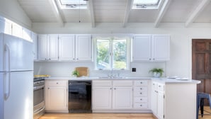 A kitchen with white cabinets, a built-in oven, and a dishwasher. - Beach Cottage (Westerly)