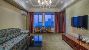 Habitación de hotel con sofá, mesa de centro, televisor, candelabro y vista de la ciudad a través de amplios ventanales.