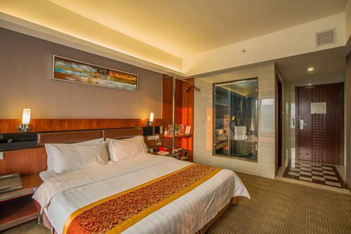 Hotelkamer met een groot bed, nachtkastje, wandtelevisie, schilderij, douchecabine van glas en een geruite vloer.
