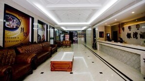 Un vestíbulo de hotel con mostrador de recepción, sofás de cuero, una mesa de centro y suelo de baldosas.
