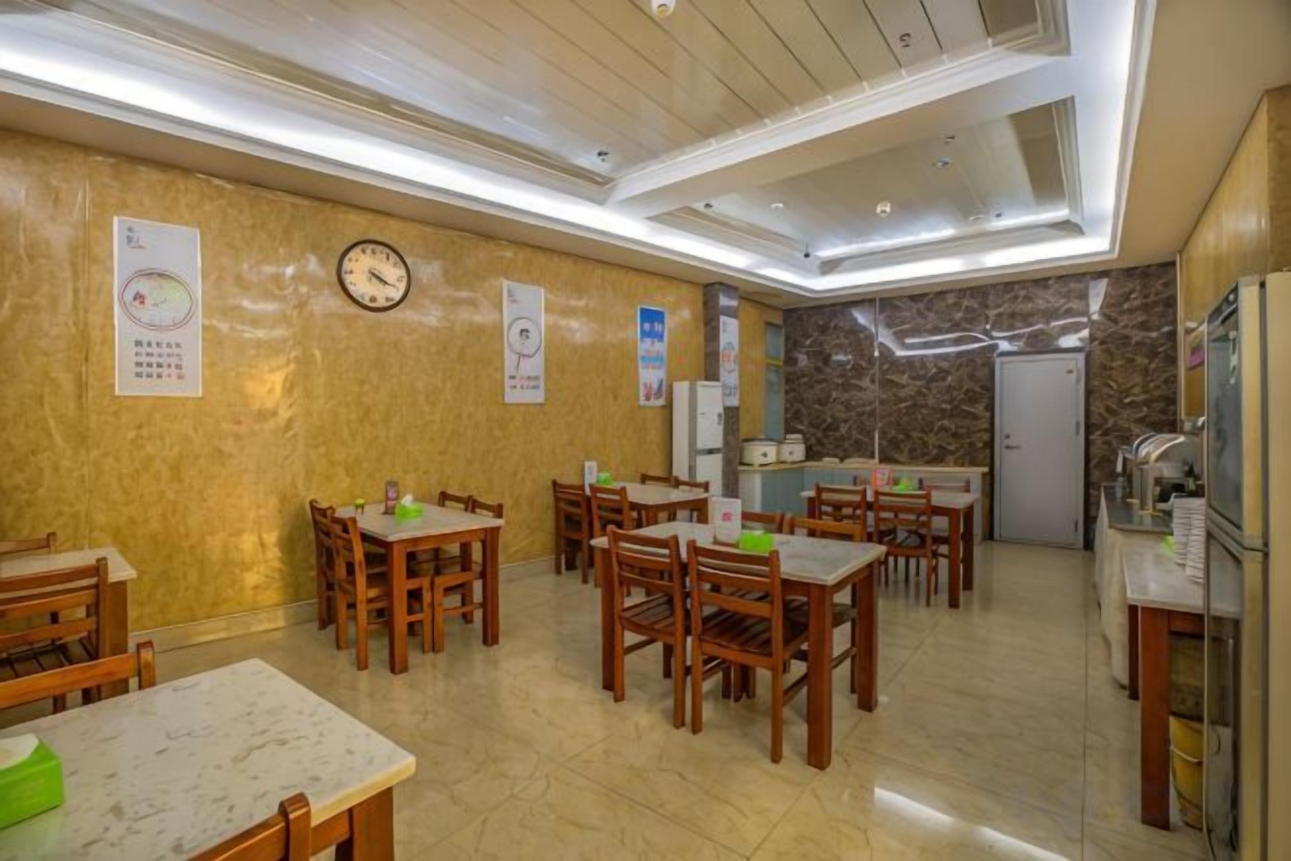 A dining area with multiple wooden tables and chairs, a clock on the wall, and a kitchen area with a refrigerator and sink.