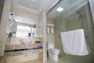 Un baño con cabina de ducha de vidrio, lavamanos con espejo e inodoro.