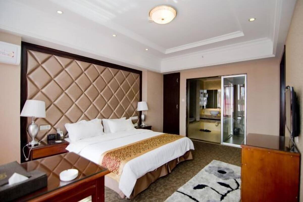 Een hotelkamer met een groot bed, twee nachtkastjes met lampen, een dressoir en een spiegel.