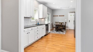 A kitchen with white cabinets, a dishwasher, and a dining area with a table and chairs. - Bright & Modern 5 BR Wintergreen Home; Minutes from Hiking, Skiing, and Wineries (Wintergreen)