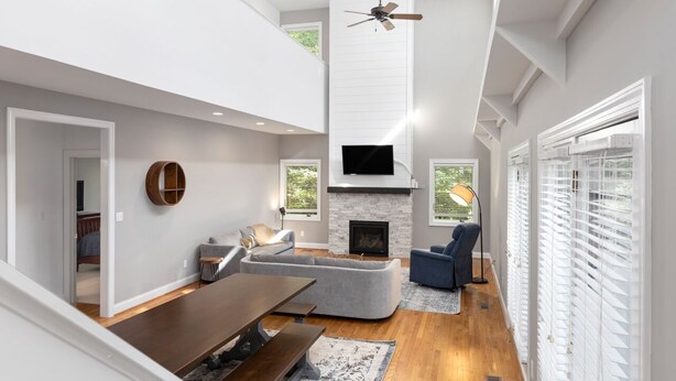 A modern living room with a fireplace, a ceiling fan, and a large window. - Bright & Modern 5 BR Wintergreen Home; Minutes from Hiking, Skiing, and Wineries (Wintergreen)
