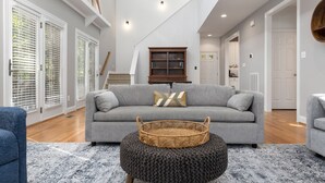 A spacious living room with a grey sofa, a wicker basket, and a patterned rug. - Bright & Modern 5 BR Wintergreen Home; Minutes from Hiking, Skiing, and Wineries (Wintergreen)