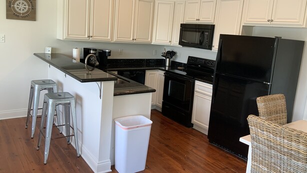 A kitchen with white cabinets, a black refrigerator, a microwave, and a stainless steel sink. - Rusty Hook located in Cypress Cove Marina   (Venice)