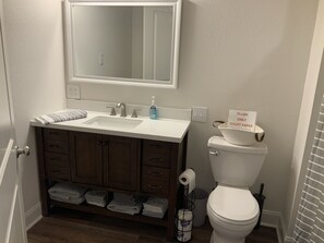 A bathroom with a white sink, dark wooden cabinets, a mirror above the sink, a toilet, and a sign on the toilet. - Rusty Hook located in Cypress Cove Marina (Venice)