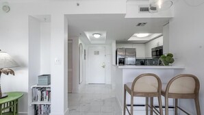 A modern kitchen with white cabinets, a stainless steel refrigerator, and a built-in oven. There is a dining area with two wicker chairs and a small table. - Coconut Grove Retreat, bayviews, 1 park incl, wkspace, Smart TV, Pool/hottub" (Coconut Grove)