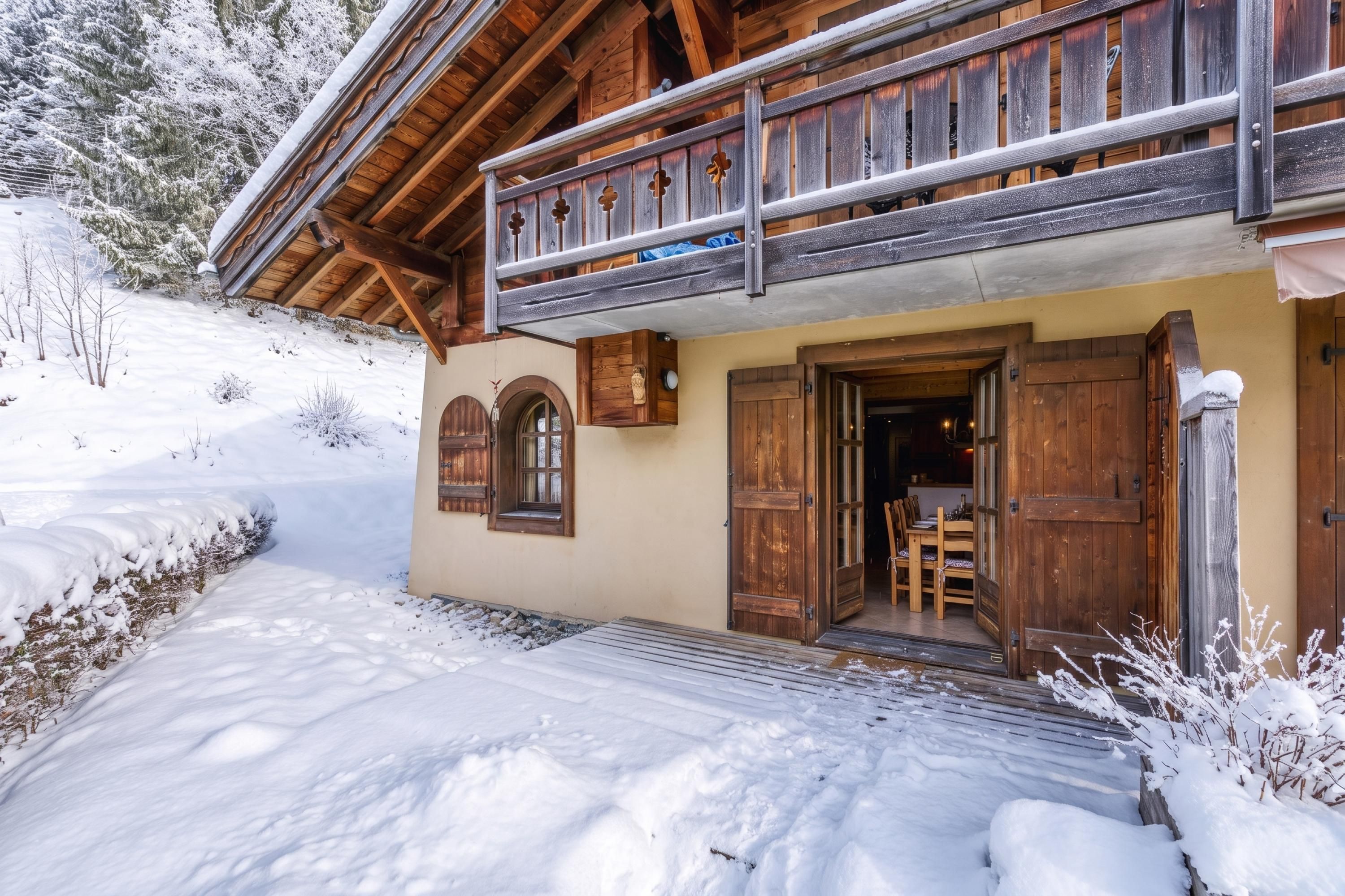 A wooden chalet with a balcony, a wooden door, and a snow-covered landscape.