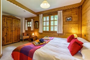 Ein Schlafzimmer einer Holzhütte mit Bett, Nachttisch, Stuhl und einem Fenster mit Vorhängen.
