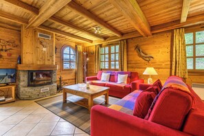 Interior de una cabaña de madera con chimenea de piedra, sofá rojo y televisor.