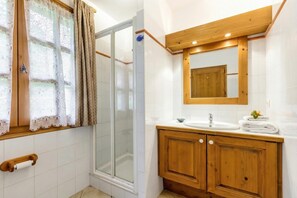 A bathroom with a shower, toilet paper holder, wooden cabinets, a sink, and a mirror. - Chalets d'Henri 67, Argentière (Chamonix), France (Argentière (Chamonix))